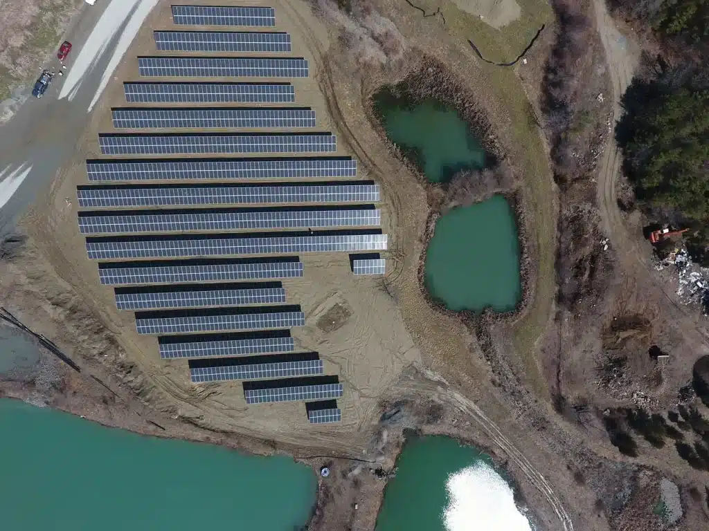 Aerial view of solar ground-mounted panels arranged in rows, surrounded by water bodies and natural landscape, showcasing BD Electrical Services' commitment to commercial solar power installations.